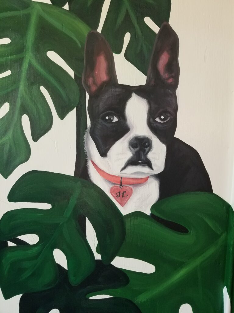 A closeup on a painting of a Boston terrier dog surrounded by large green leaves. The dog is black and white and is wearing a pink collar with a heart-shaped pendant on it, and the heart contains a stylized letter H.